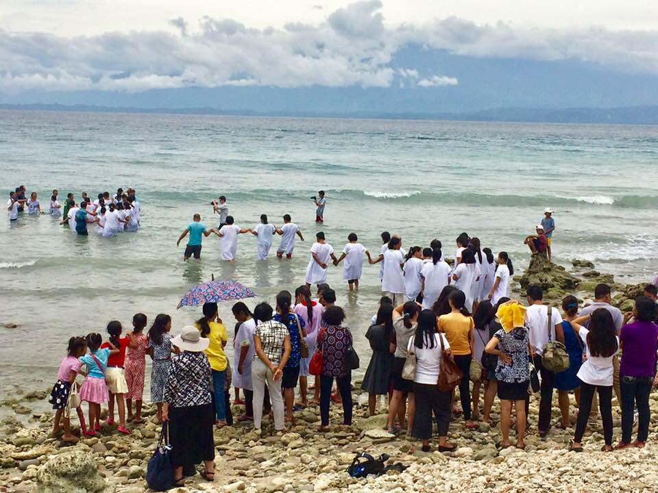 A PAMAS ministry team holds a mass baptism in the sea, with people watching and singing on the shore.