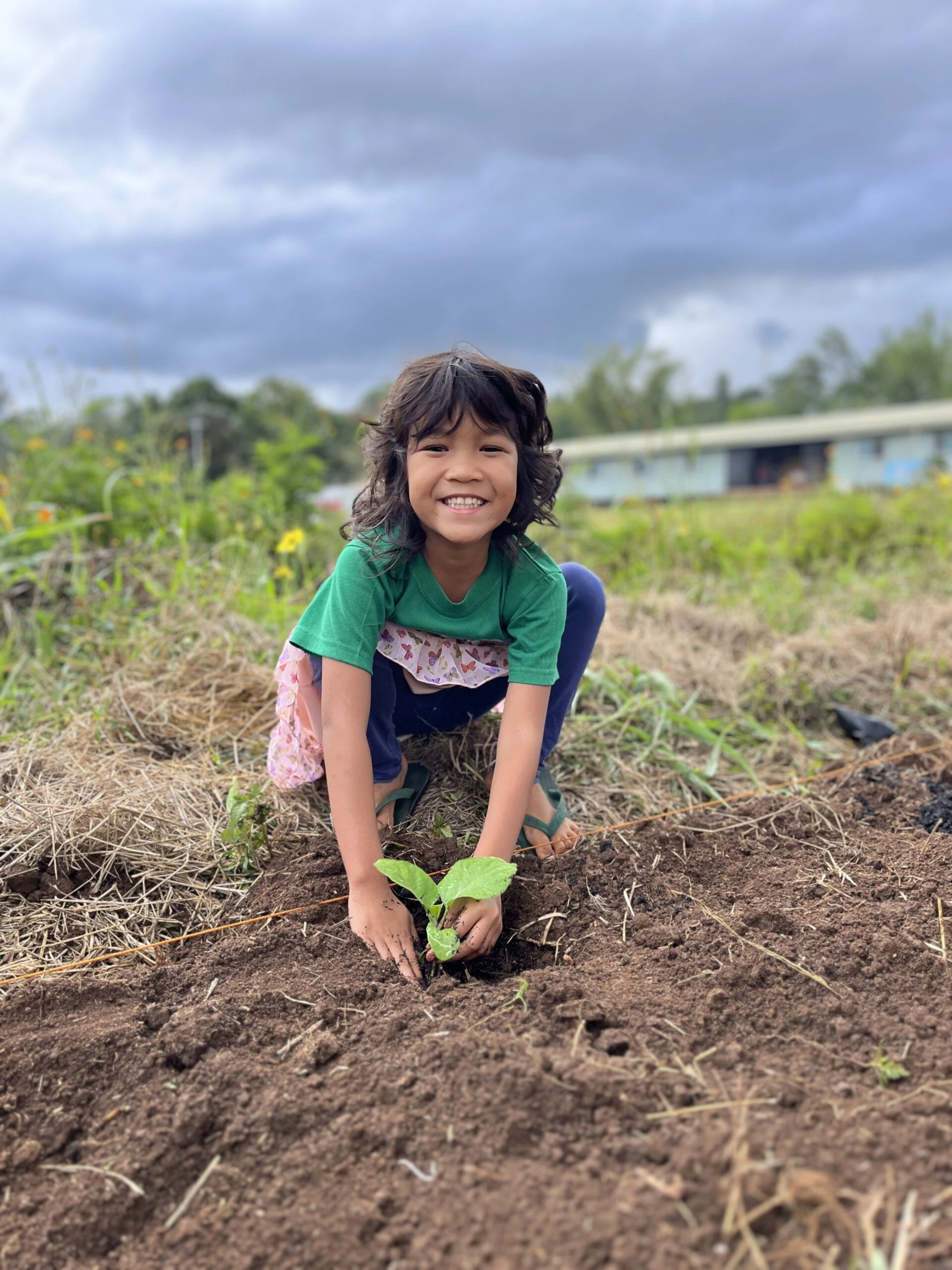 Young child in the Philippines smiling while planting, participating in PAMAS Mission's community agriculture education.